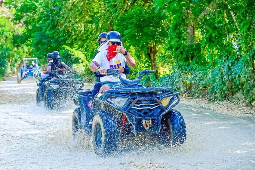 People riding ATVs on a dirt road surrounded by greenery. 1