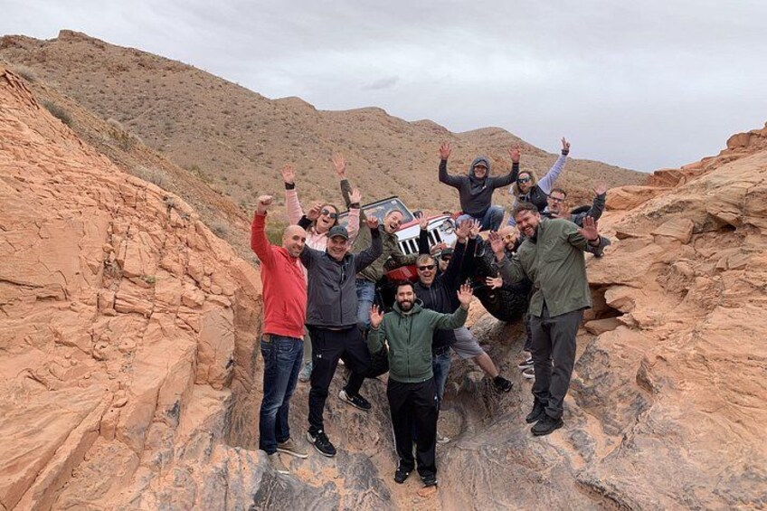 A group of people posing with a vehicle in a rocky desert landscape. 5