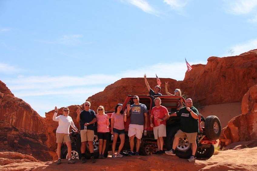 A group of people posing with a red off-road vehicle in a desert canyon. 4