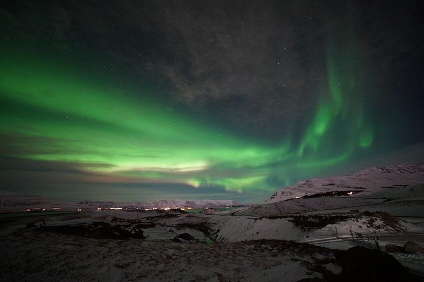 The Northern Lights over a snowy landscape with distant buildings. 4