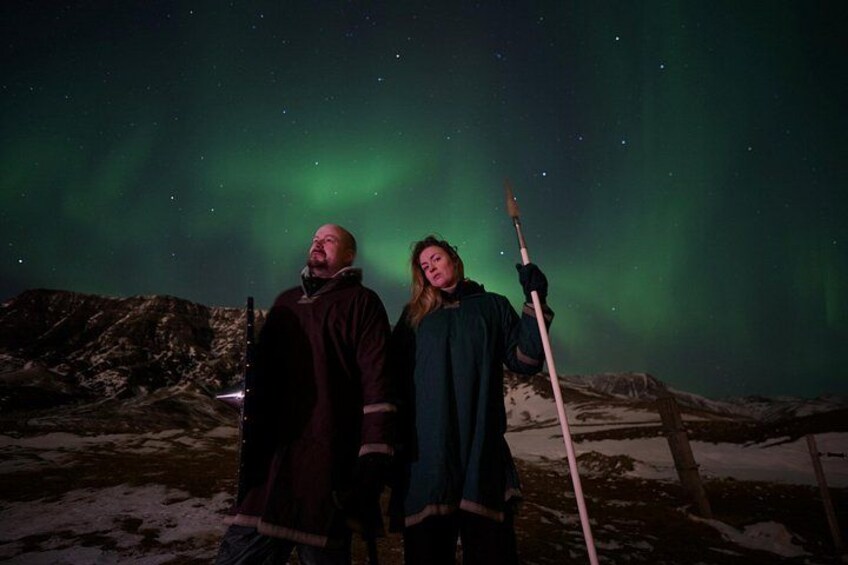 Two people standing on a snowy landscape under a starry night sky with the aurora borealis. 2