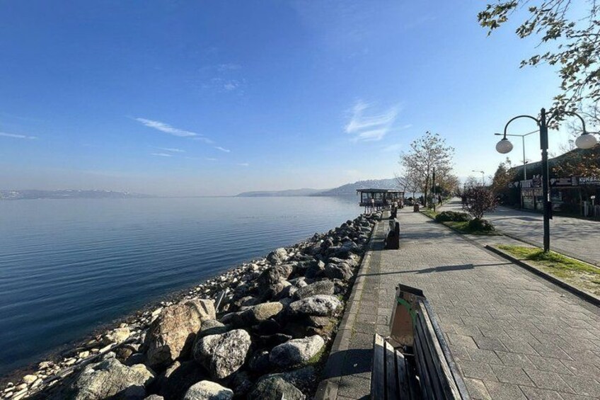 A waterfront promenade with a rocky shoreline, benches, and street lamps. 3
