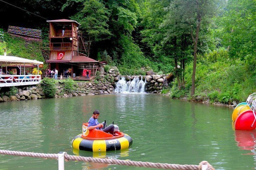 Una persona en un bote colorido en un río tranquilo, rodeada de exuberante vegetación y una pequeña cascada. 3