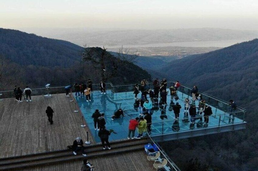 A glass-bottomed pool surrounded by people on a wooden deck with a mountainous landscape in the background. 5
