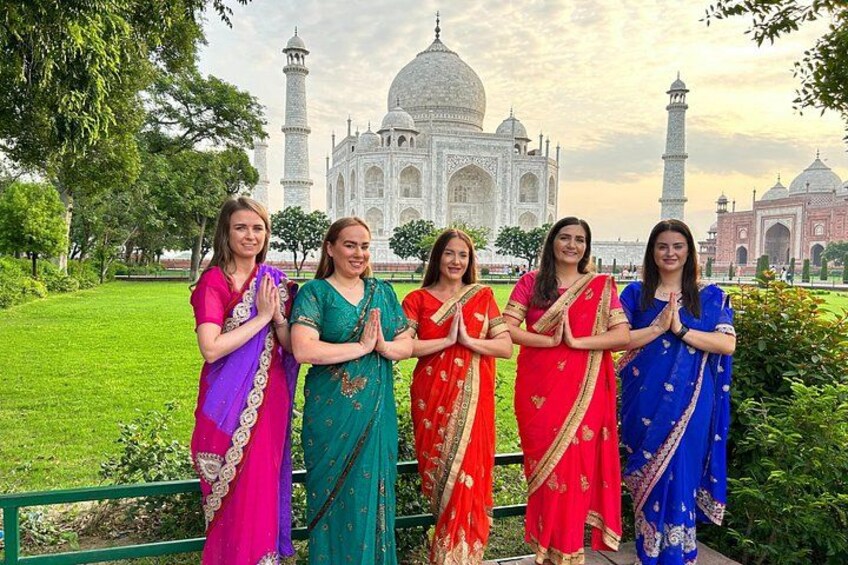 Un groupe de femmes, vêtues de costumes traditionnels aux couleurs vives, se tient devant le Taj Mahal. 3