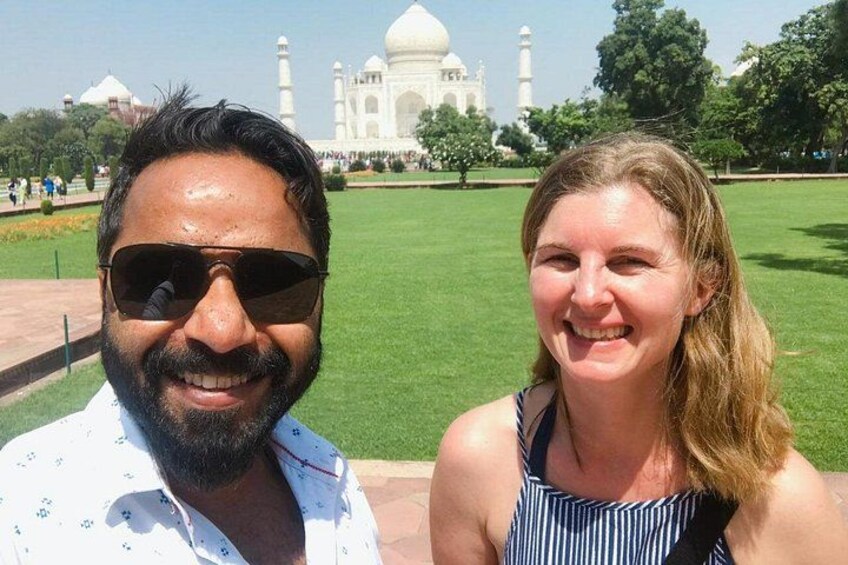 Deux personnes se tiennent devant le Taj Mahal, avec une pelouse verte et des arbres en arrière-plan. 2
