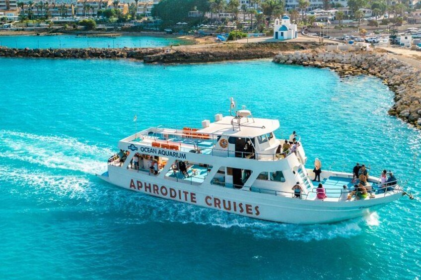 En hvid båd med navnet 'Aphrodite Cruises', hvor der står 'Ocean Aquarium' på, sejler på turkisblåt vand. 1