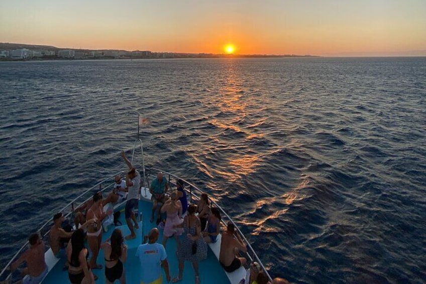 A boat with people enjoying a sunset over the water. 5