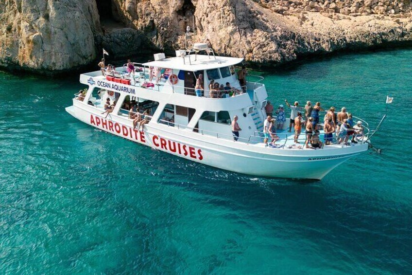 A white boat named 'Aphrodite Cruises' with 'Ocean Aquarium' written on it, sailing on turquoise water near rocky cliffs. 4