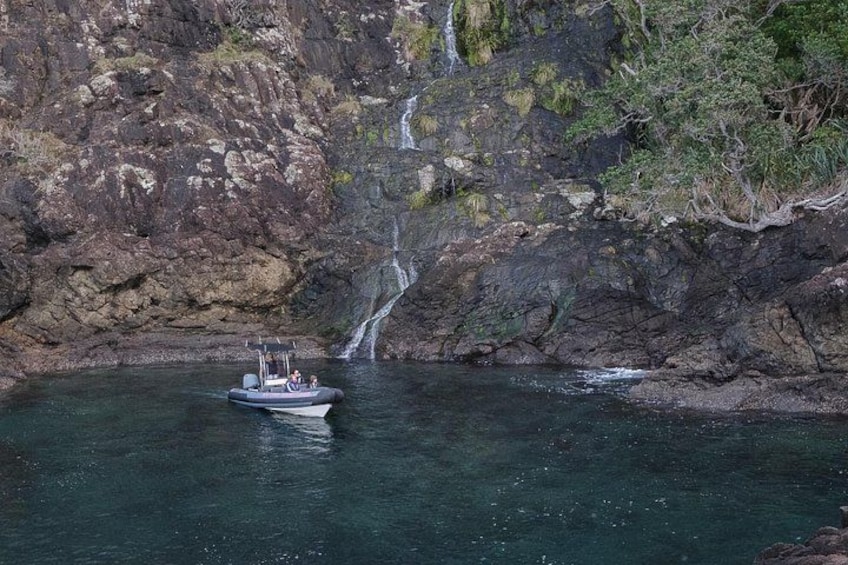 A boat on calm water near a rocky cliff with a waterfall. 2