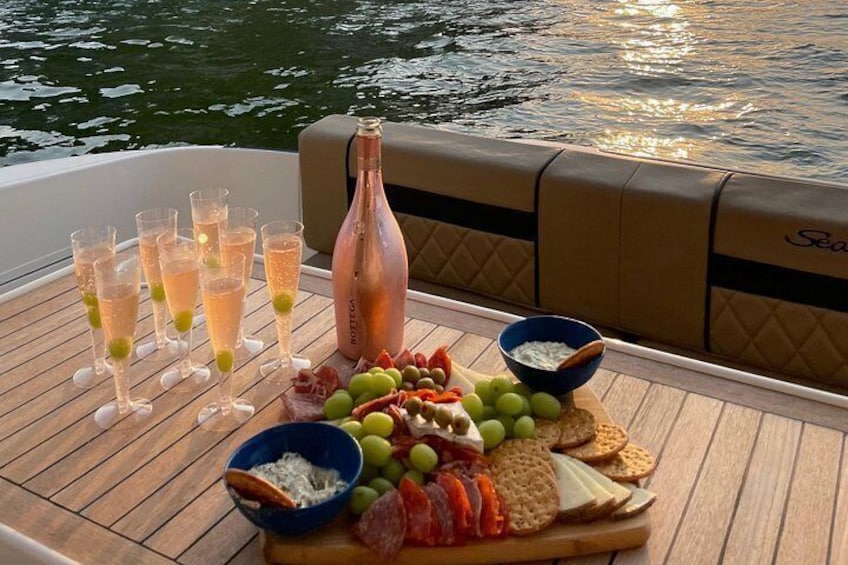 A boat with a table set with glasses of champagne, a bottle, and a charcuterie board with fruits and crackers. 1