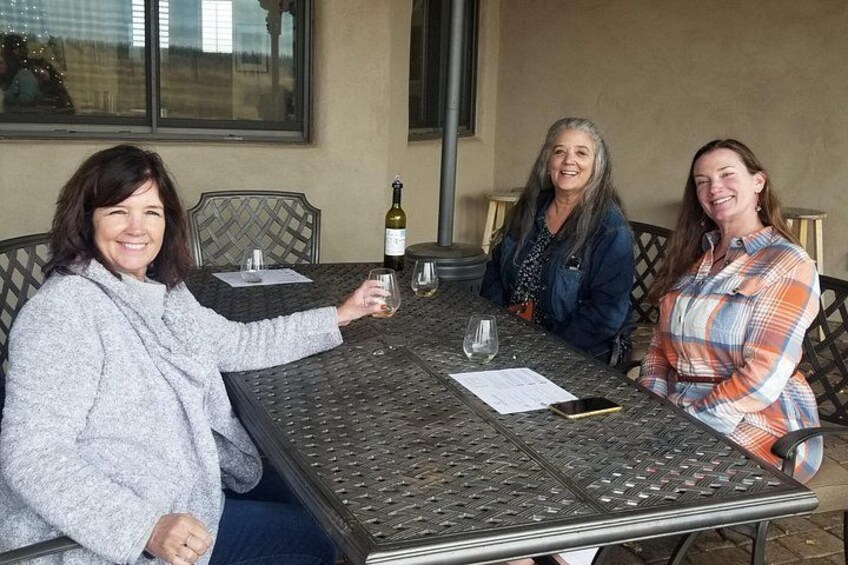 Three people sitting at a table with a bottle of wine and glasses. 4