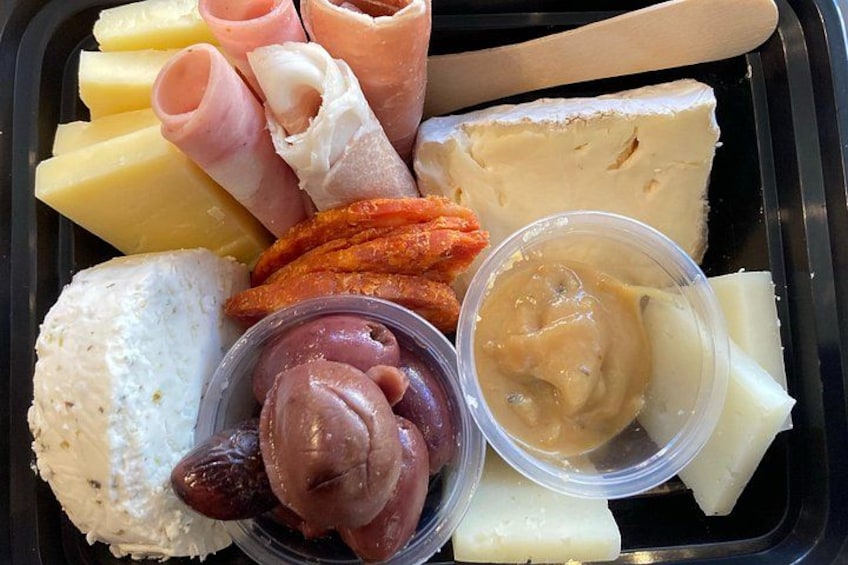 A variety of cheeses, meats, and dips in a black container. 3