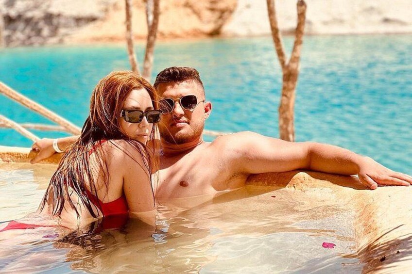 Un couple se détend dans une source thermale aux eaux d’un bleu cristallin, entouré d’arbres et d’un paysage rocheux. 3