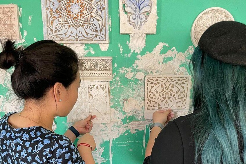 Twee personen bekijken gedetailleerde wanddecoraties. 1