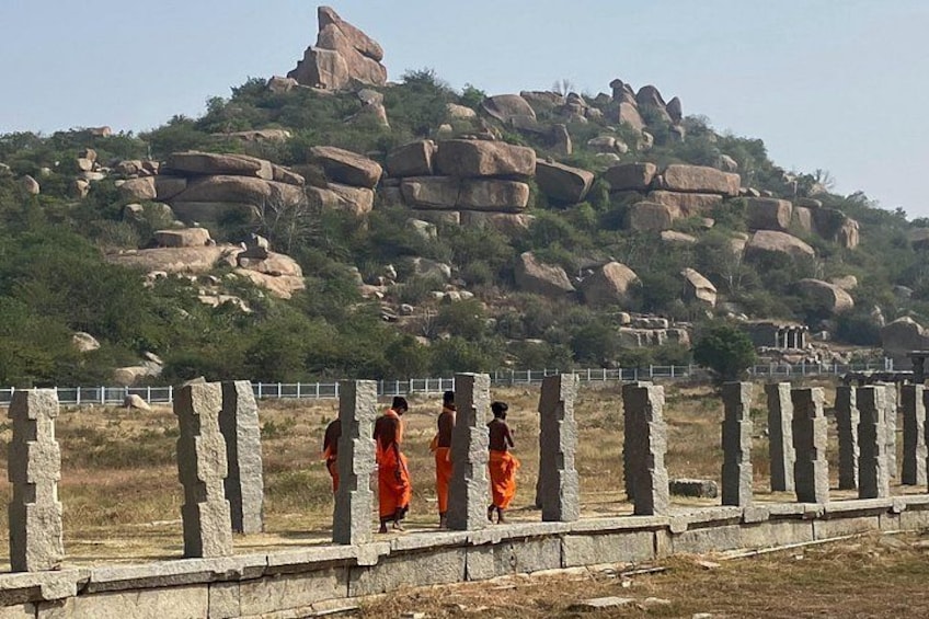 A group of people in orange robes walking along a stone pathway with a large rock formation in the background. 5
