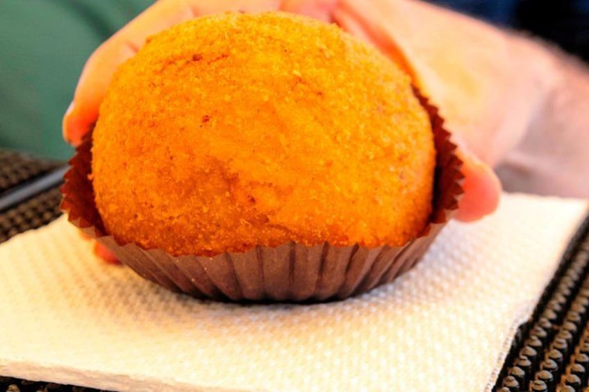 A hand holding a golden-brown muffin in a paper cup. 1