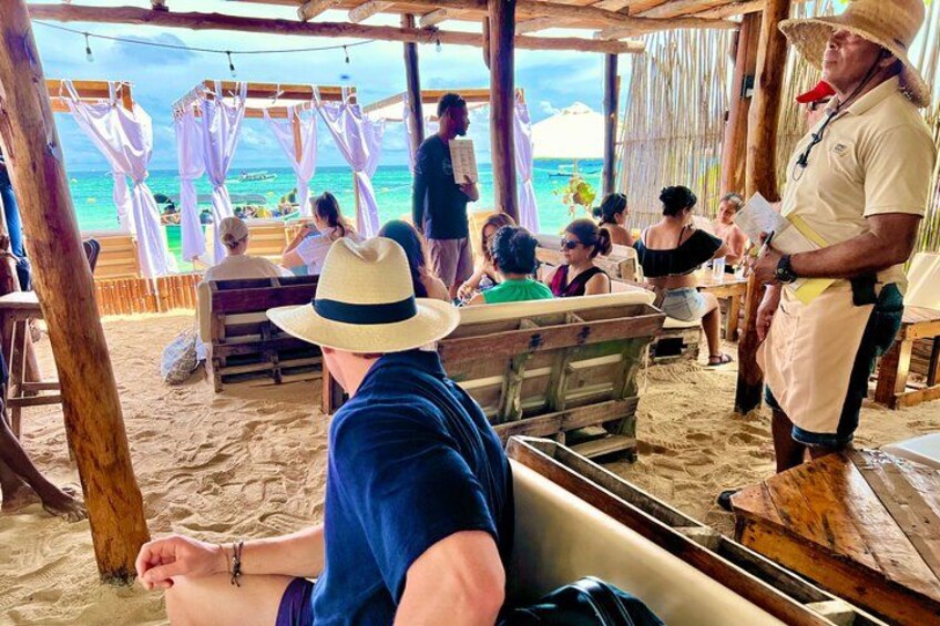 A beachside event with wooden structures and people seated on benches. 2
