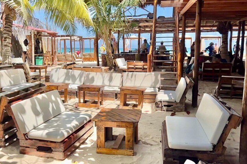 Un espacio de descanso frente al mar con mobiliario de madera y palmeras. 2
