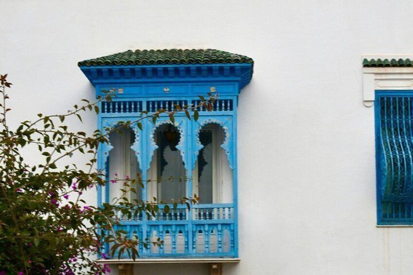 A blue wooden balcony with intricate carvings and a green tiled roof. 2