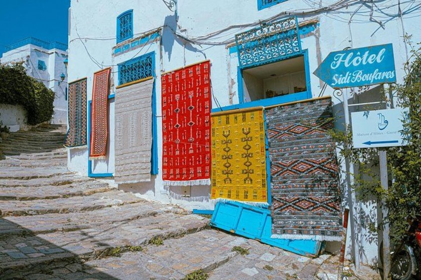 Un edificio blanco con contraventanas de colores, un letrero que dice 'Hotel Sidi Boufaires' y una calle adoquinada. 5