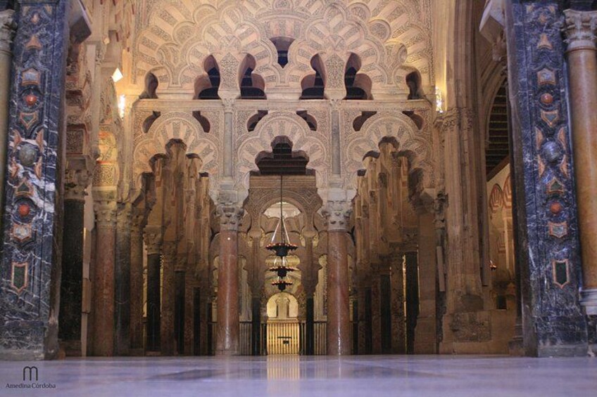 An interior with ornate arches and columns, a chandelier, and a patterned floor. 3
