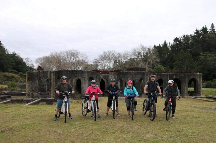 A group of cyclists standing in a grassy area with a stone structure in the background. 5