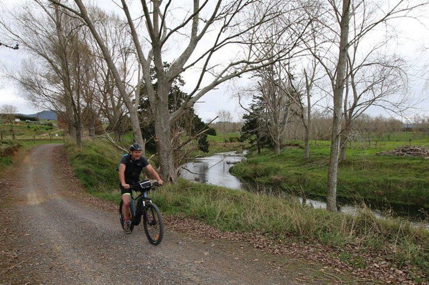 A cyclist on a gravel path with a stream and trees in the background. 2
