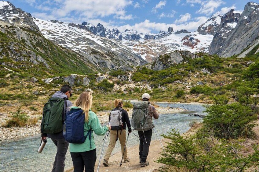 Un groupe de randonneurs sur un sentier de montagne, avec une rivière, des sommets enneigés et une végétation clairsemée. 4