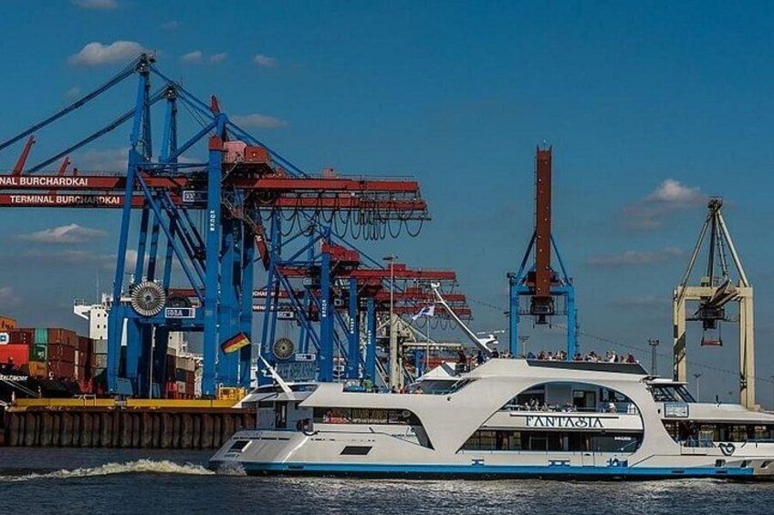 De veerboot Fantasia is afgemeerd in een haven met grote, blauwe kranen en in de verte vrachtcontainers. 2