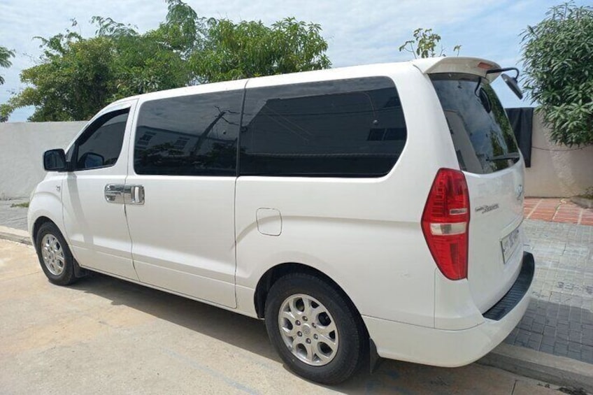 A white van parked on a paved area with a curb, trees, and a clear sky in the background. 1