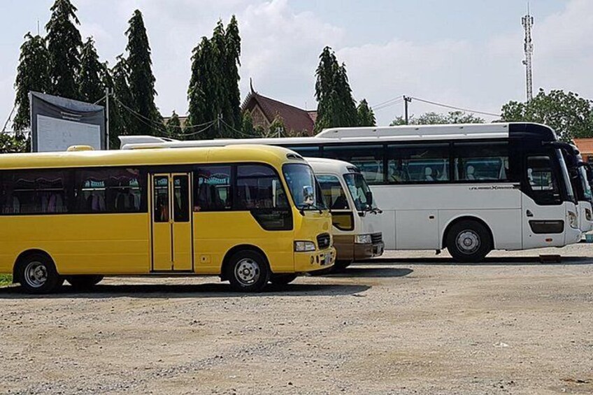 Twee bussen op een grindpad, met bomen en een gebouw op de achtergrond. 5