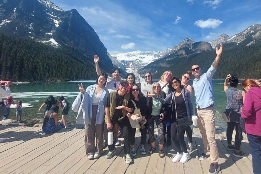 Un grupo de personas en un muelle de madera junto a un lago, con montañas al fondo. 3