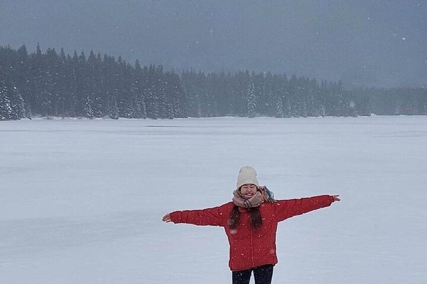 A person in a red jacket and white hat standing with arms outstretched in a snowy landscape. 4