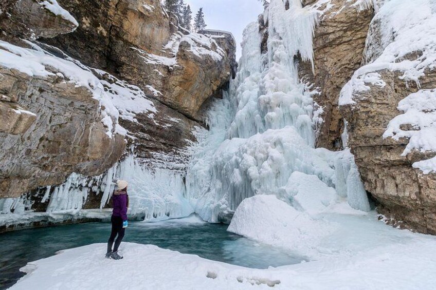 Una persona de pie sobre una roca cubierta de nieve cerca de una cascada congelada. 3