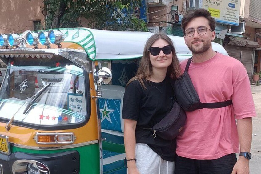 A couple standing in front of a colorful auto-rickshaw with a star design and a sign that reads 'My Book Pink City.' 3