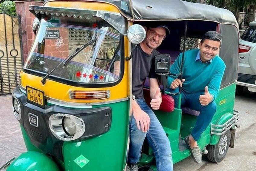 Two men sitting in a green and yellow auto-rickshaw. 1
