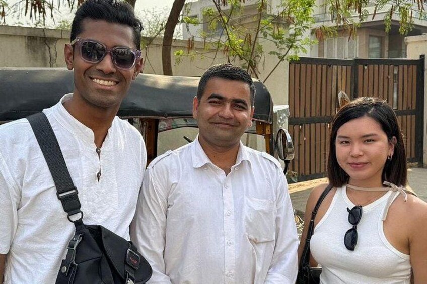 Three people standing outdoors with a vehicle and a fence in the background. 4