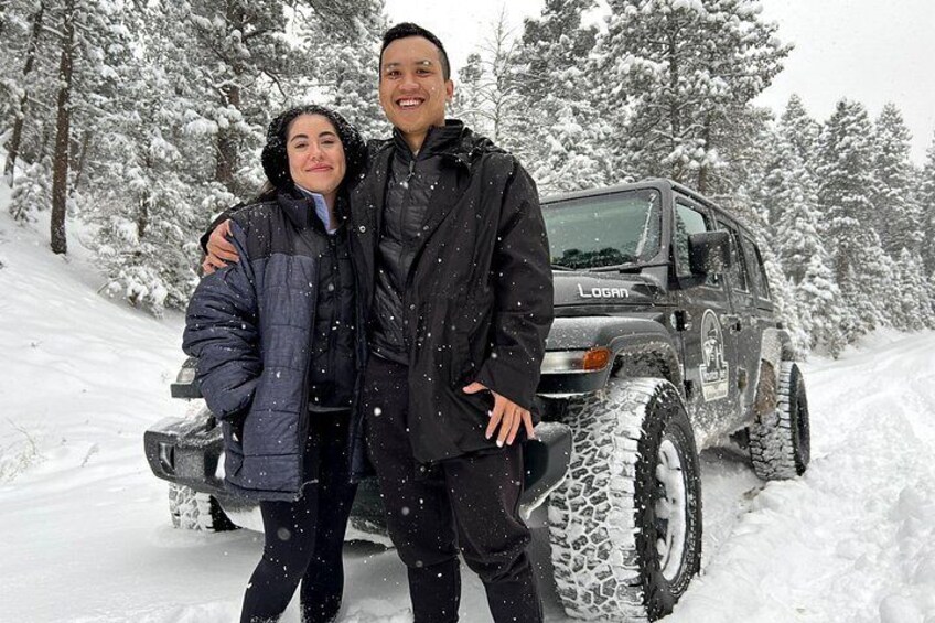 A couple standing in front of a snow-covered SUV in a snowy forest. 4
