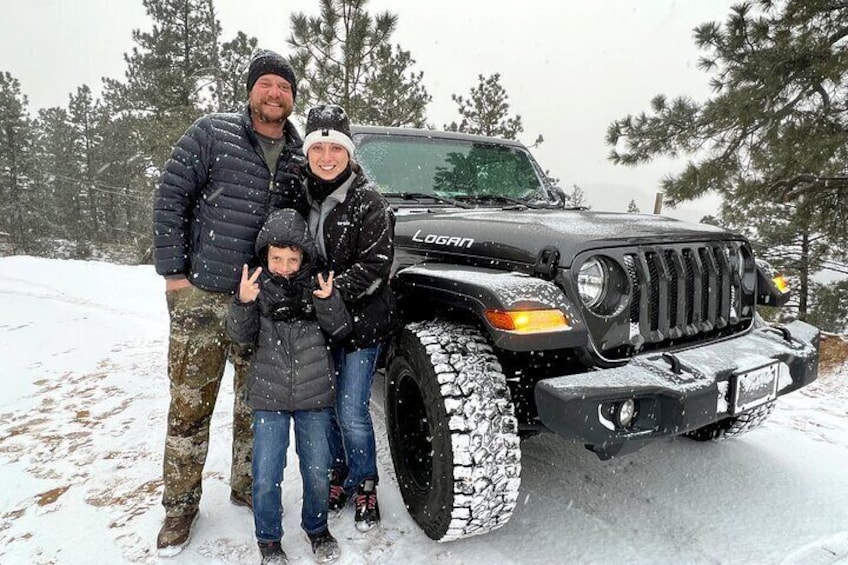 A family posing with a black off-road vehicle in a snowy landscape. 2