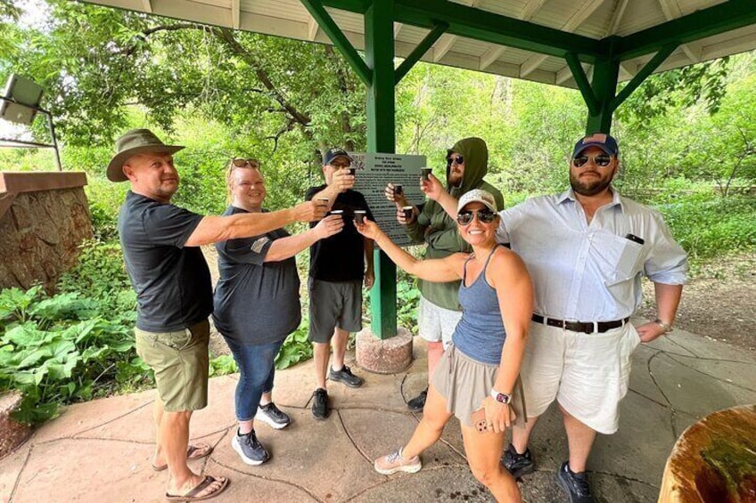 A group of people taking a selfie at a park with a green pavilion and trees in the background. 3