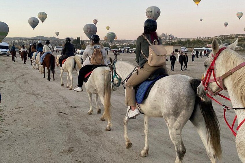 People riding horses on a dirt path with hot air balloons in the background. 2