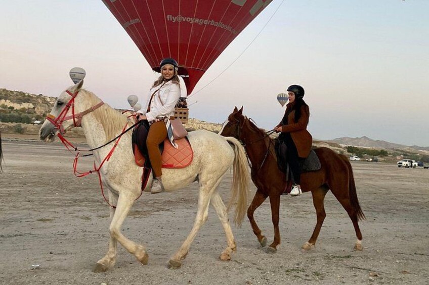Two people riding horses with a red hot air balloon in the background. 3