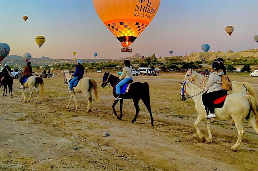 People riding horses in a field with hot air balloons in the background. 4