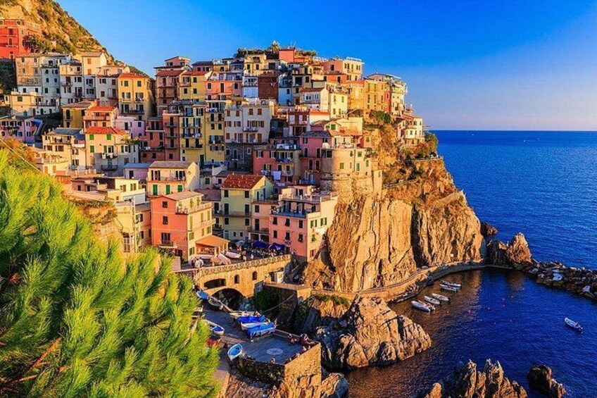 A coastal village with colorful buildings perched on a cliff, a bridge, and boats in the water. 1