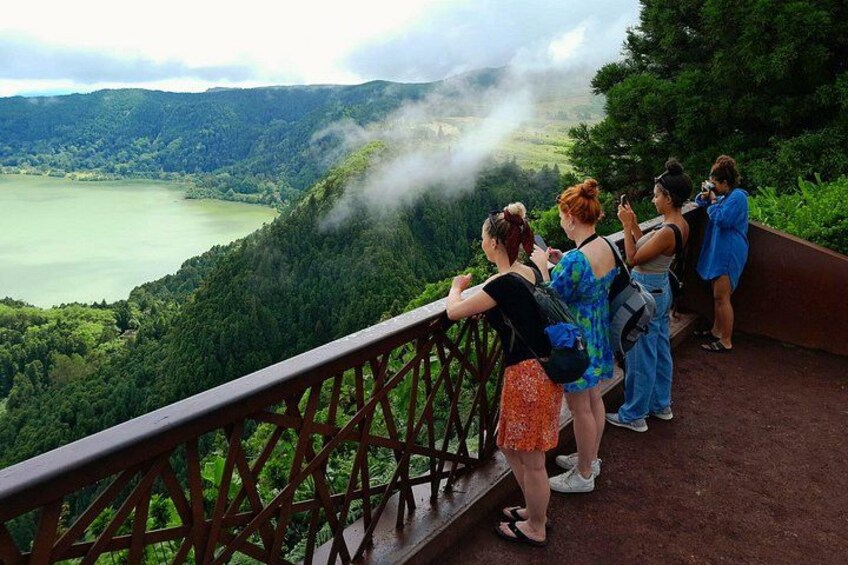 A group of people on a viewing platform overlooking a lake surrounded by forested hills. 4