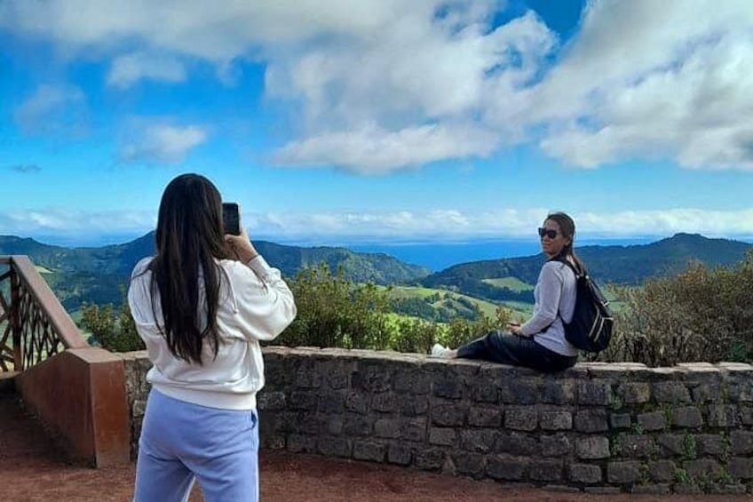 Two people sitting on a stone wall overlooking a mountainous landscape. 2