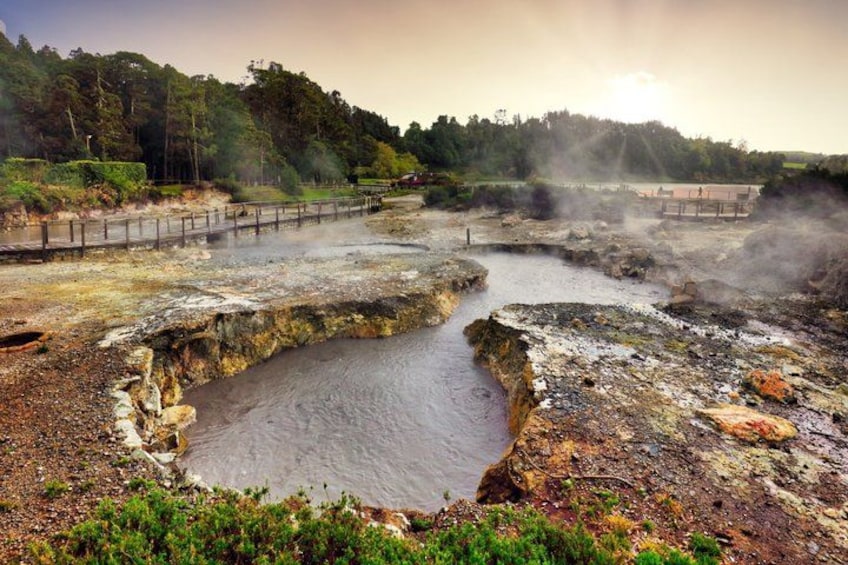 A geothermal area with steam vents, a water body, and a wooden walkway. 1