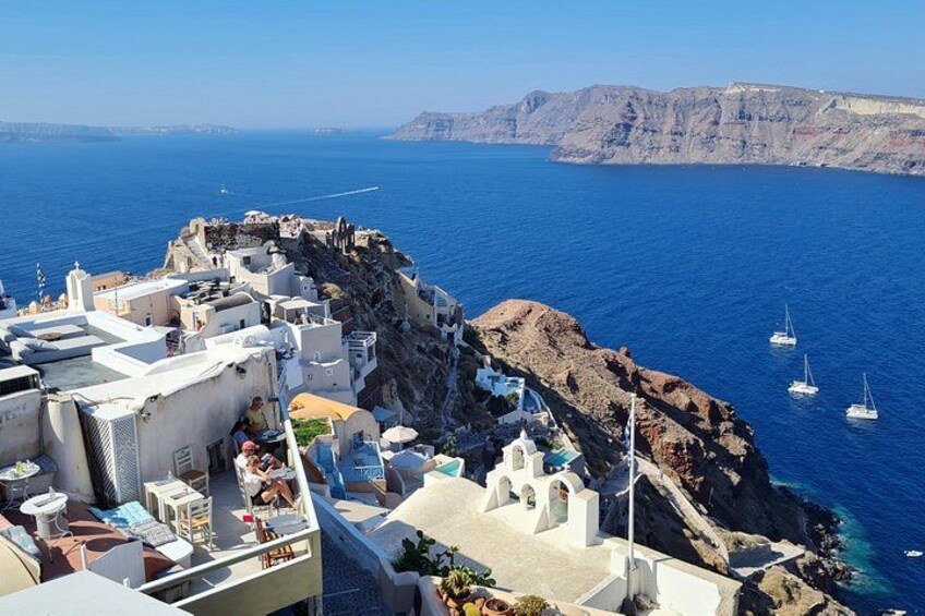 A coastal village with white buildings, rocky cliffs, and sailboats on the sea. 5