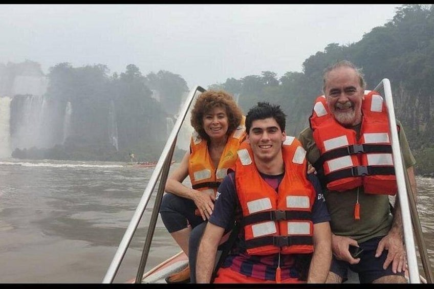Un grupo de personas en un bote, usando chalecos salvavidas, con una cascada al fondo. 2